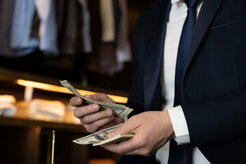 Close-up businessman counts US dollars while sitting on a chair in a clothing store