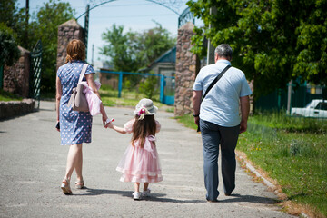 family walking in the park. mom dad and little girl walking holding hands. back view. daughter in a pink dress. friendly loving family concept, love. outdoor, walk in the fresh air, threesome