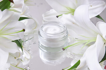 Obraz na płótnie Canvas Cream for skin care, natural cosmetics made of flowers and petals. A glass jar of white cream stands among the lily flowers