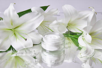 Fototapeta na wymiar Cream for skin care, natural cosmetics made of flowers and petals. A glass jar of white cream stands among the lily flowers
