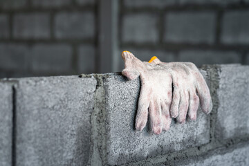 A pair of dirty cotton glove for building worker is hanging on the brickwall during the staff taking a rest. Industrial object photo. Partail focus at the glove part