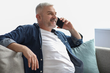 Relaxed mature man sitting on couch and talking on phone