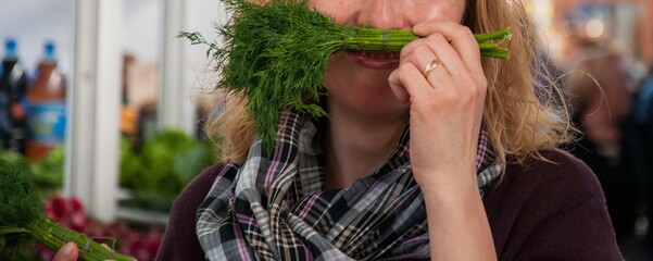 Female hand holds bunch of fresh dill greenery like mustache near mouth. Unrecognizable smiling woman with greens at local veggie market outdoor