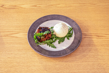 burrata with pepper, arugula, olives, tomato and basil on a blue and white plate