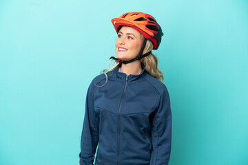 Young cyclist woman isolated on blue background thinking an idea while looking up