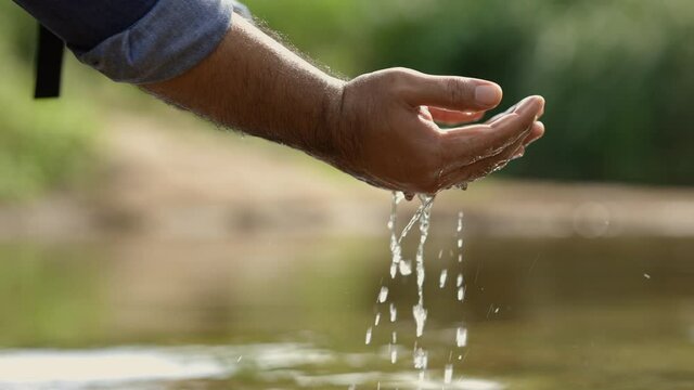 Closeup water drops falling down from man hand at river in mountains.Hand touching fresh water. Happy freedom concept.