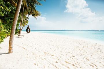 Azure coast of Maldives. Beach with palm trees, white sand, swing on the beach