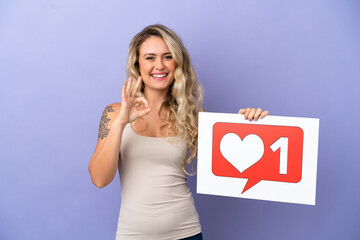 Young Brazilian woman isolated on purple background holding a placard with Like icon and celebrating a victory