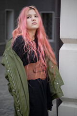 a girl with long pink hair stands and looks to the side, she is wearing a Basco belt