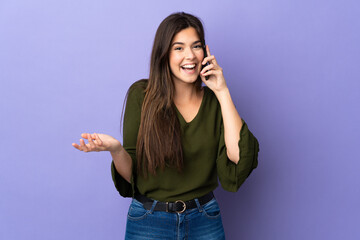 Teenager Brazilian girl over isolated purple background keeping a conversation with the mobile phone with someone