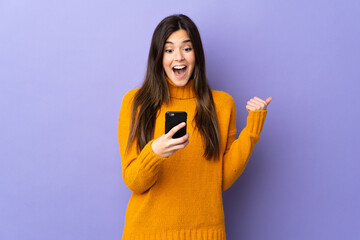 Teenager Brazilian girl over isolated purple background surprised and sending a message
