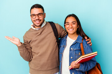 Young mixed race student couple isolated on blue background showing a copy space on a palm and holding another hand on waist.