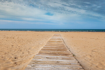 Fototapeta na wymiar Wooden walkway extended on a fine sandy beach with the Mediterranean Sea in the background.