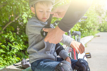 Father dad putting protection elbow pads and knee pads for cycle on his son. Help and caring for...