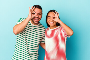 Fototapeta premium Young mixed race couple isolated on blue background excited keeping ok gesture on eye.