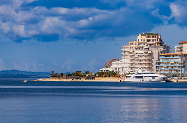 Panoramic view of Saranda bay and town and hotels along the coast, Albania. Sunny summer day. Beautiful clouds in the sky. Albanian mountains visible on the horizon. Calm blue sea.