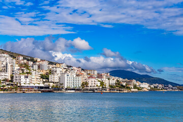Panoramic view of Saranda bay and town and hotels along the coast, Albania. Sunny summer day. Beautiful clouds in the sky. Albanian mountains visible on the horizon. Calm blue sea.