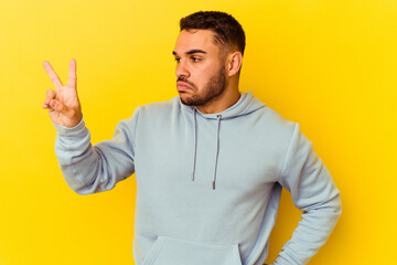 Young caucasian man isolated on yellow background joyful and carefree showing a peace symbol with fingers.