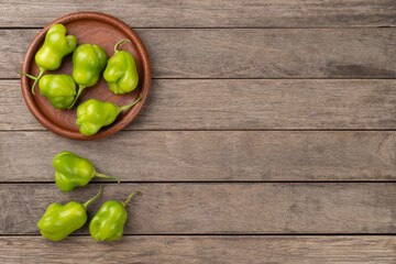 Green cambuci peppers on a plate over wooden table with copy space