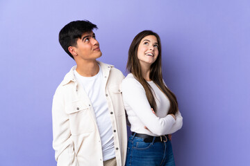 Young couple over isolated purple background looking up while smiling
