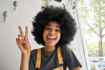 Young happy African American generation z student female hipster recording vlog indoor. Webcam view of smiling teenage beauty blogger influencer speaking to friend online in virtual video call.