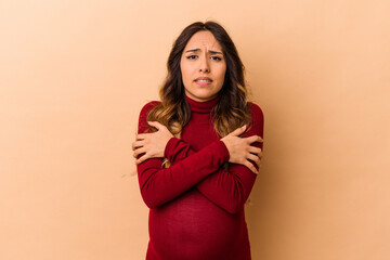 Young mexican pregnant woman isolated on beige background going cold due to low temperature or a sickness.