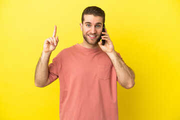 Handsome blonde man using mobile phone over isolated background pointing up a great idea