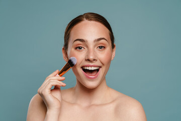 Half-naked ginger woman smiling and using cosmetic brush