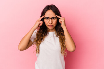 Young mexican woman isolated on pink background focused on a task, keeping forefingers pointing head.