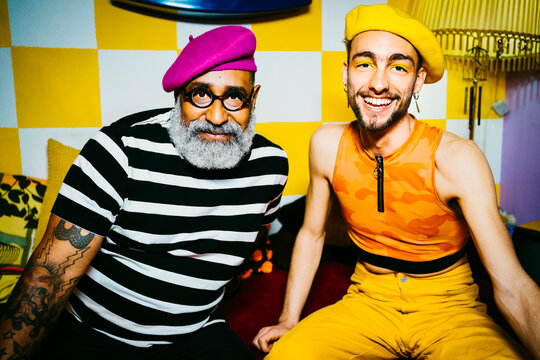 Smiling young man with senior male friend wearing berets sitting in living room