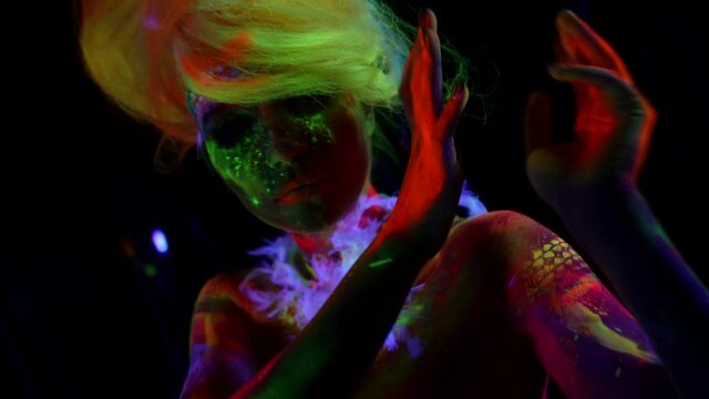 mysterious woman with fluorescent paints on skin is moving in darkness