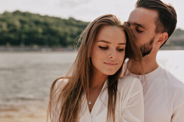 Obraz premium Sensitive pretty girl with long light-brown hair smiling while her boyfriend is kissing her on the sandy beach