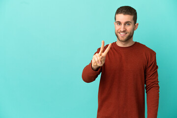 Handsome blonde man over isolated blue background smiling and showing victory sign