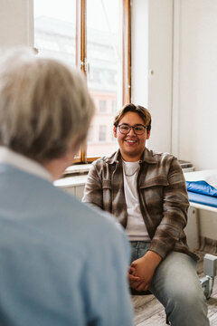 Smiling male patient looking at senior female medical expert during consultation in clinic