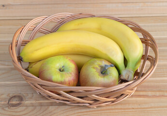 Some bananas and apples in a basket - Wooden Background