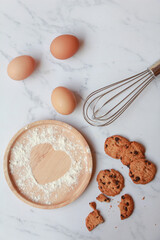 Heart of the flour on wooden plate with eggs and cookies on marble background. prepation for cooking homemade cookise. top view, love concept. 