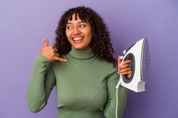 Young mixed race woman holding an iron isolated on purple background showing a mobile phone call gesture with fingers.