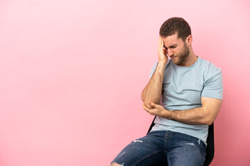 Obraz premium Young man sitting on a chair over isolated pink background with headache