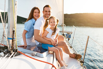Cheerful Family Of Three Relaxing Embracing Sitting On Yacht Deck