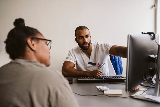 Male healthcare worker discussing over computer with female patient in medical clinic