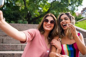 Two friends taking selfie with phone outdoors.