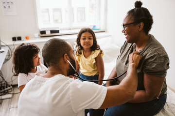 Male healthcare worker with stethoscope examining smiling woman looking at daughter