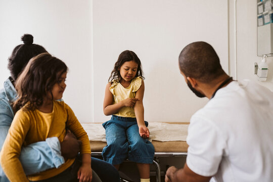 Girl talking with male doctor while pointing at hand in medical clinic