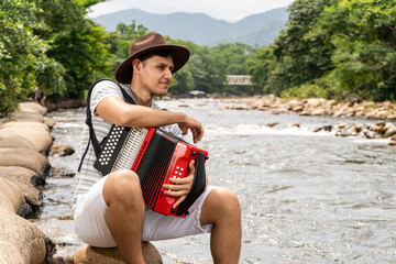 Joven tocando el acordeon a orillas del rio guatapuri en valledupar - obrazy, fototapety, plakaty