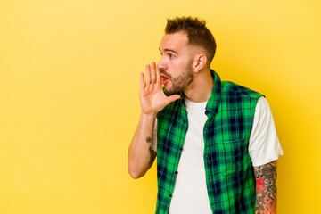 Young tattooed caucasian man isolated on yellow background is saying a secret hot braking news and...