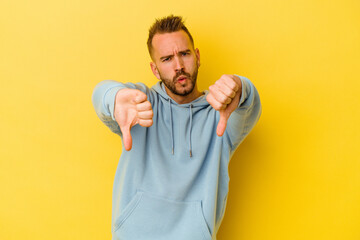 Young tattooed caucasian man isolated on yellow background showing thumb down and expressing...