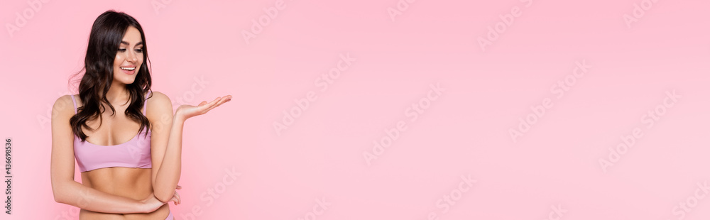 Wall mural young woman in top of swimsuit pointing with hand isolated on pink, banner.