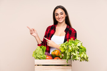 Farmer with freshly picked vegetables in a box isolated on beige background pointing finger to the side