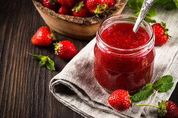 Strawberry jam in the glass jar with fresh berries at wooden table.