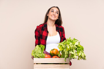 Farmer with freshly picked vegetables in a box isolated on beige background laughing and looking up